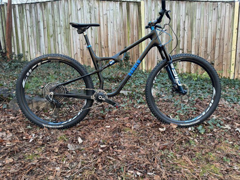 Black Cobalt full-suspension mountain bike beside a wooden fence